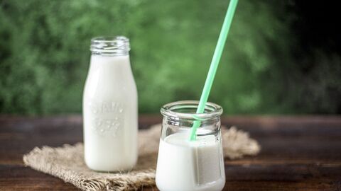 Eine Glasflasche und ein Glas mit Strohhalm sind mit Milch gefüllt und stehen auf einem Holztisch. 