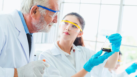 Eine junge Laborantin zeigt ihrem Ausbilder das Ergebnis ihres Versuches in einem Reagenzglas