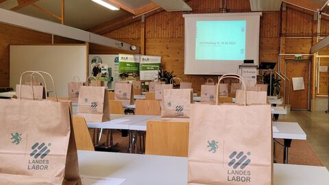 Internationale Arbeitsgemeinschaft für Futtermittelanalytik (IAG) Sektion Futtermittelmikroskopie tagte In einem Tagungsraum sind Tische für eine Veranstaltung aufgestellt. Auf den Tischen stehen Papiertüten mit dem Logo des Landeslabor