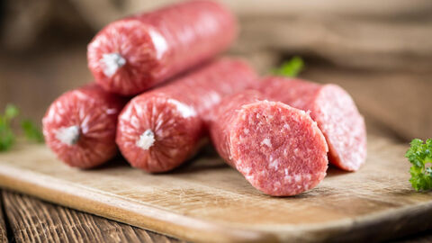 Auf einem Holzbrettchen liegen frische Mettwürstchen. Eine Wurst ist aufgeschnitten.