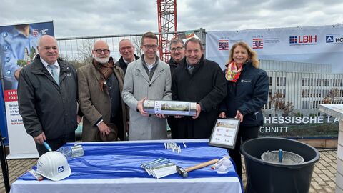 v.l.n.r.: Thomas Platte, Direktor, Landesbetrieb Bau und Immobilien Hessen, Prof. Johannes Kister, Gesellschafter kister scheithauer gross architekten und stadtplaner GmbH, Hartmut Römer, Direktor, Landesbetrieb Hessisches Landeslabor, Michael Ruhl, Staatssekretär, Hessisches Ministerium für Landwirtschaft und Umwelt, Weinbau, Forsten, Jagd und Heimat, Mark Weinmeister, Regierungspräsident Kassel, Prof. Dr. R. Alexander Lorz, Staatsminister, Hessisches Ministerium der Finanzen, Sandra Arendt, Niederlassungsleitung Soziale Infrastruktur Europa, HOCHTIEF PPP Solutions Es stehen verschiedene Personen vor einem Podest, auf dem Utensilien stehen, die mit in die Zeitkapsel gepackt wurden und die dem Bau des Hauses dienlich sind.