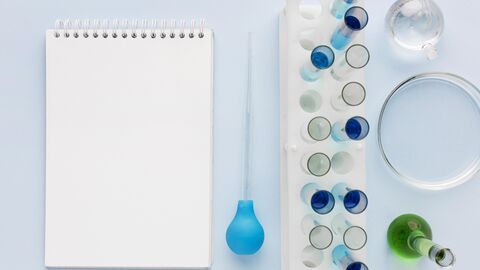 Ein Block liegt auf einer Tischfläche. Daneben stehen unterschiedliche Reagenzgläser und eine Petrischale. 