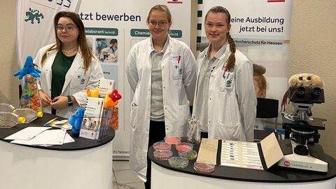 Drei Auszubildene stehen am Messestand des Landeslabor vor zwei Roll-Up-Displays und hinter kleinen Messeständen