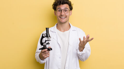 Junger Mann mit einem Mikroskop schaut in die Kamera