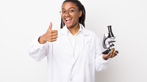 Junge Frau mit einem Mikroskop lacht in die Kamera