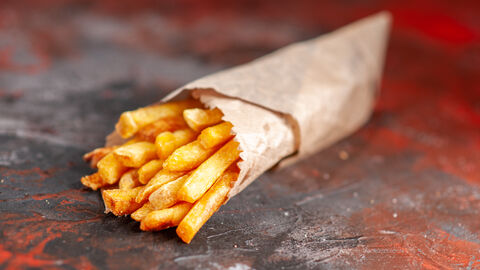 Eine Tüte Pommes Frites liegt auf einem Holztisch 