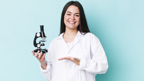 Junge Frau mit Mikroskop in der Hand lächelt in die Kamera