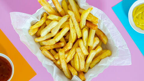 Ein größere Schale mit Pommes frites und zwei kleine Schälchen mit Senf und Ketchup auf einer glatten farbigen Oberfläche