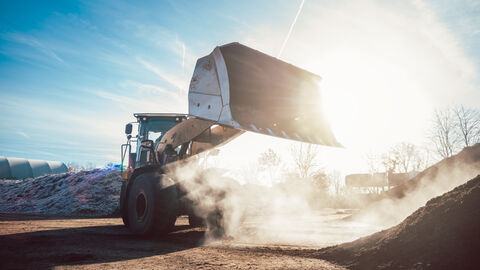 Ein Bagger setzt große Komposthaufen von Bioabfall um