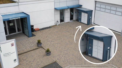 Vorplatz des Haupteingangs des Landeslabors. Es sind eine beschriftete Stele, der Haupteingang und der Probeautomat inklusive einer Vergrößerung zu sehen.